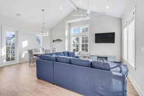 Ein geräumiges Wohnzimmer mit einem großen blauen Ecksofa, einem Essbereich mit Korbstühlen und einem Deckenventilator.