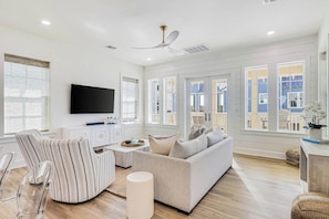 A spacious living room with a large flat-screen TV, a sofa, a striped chair, and a wooden coffee table. - Sunsets And Smiles| Resort and Beach Access (Port Aransas)
