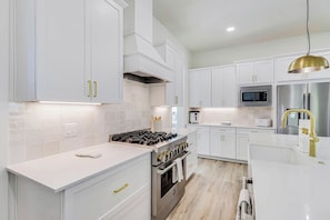 A modern kitchen with white cabinetry, stainless steel appliances, and a gold pendant light. - Sunsets And Smiles| Resort and Beach Access (Port Aransas)