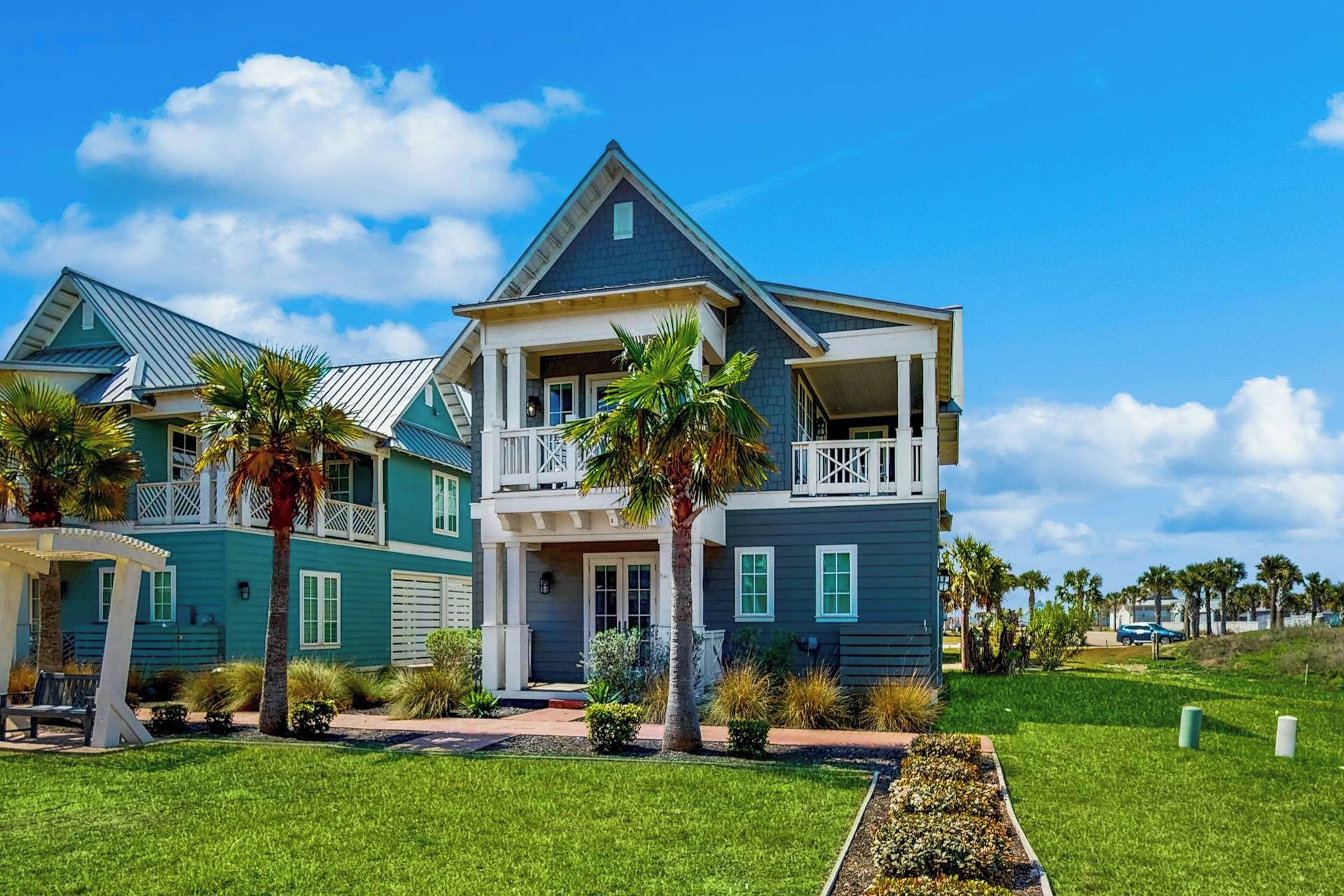 A two-story house with a balcony, surrounded by well-maintained lawns and palm trees.