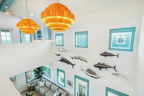A multi-level interior with a dining area, a living room with a sofa, and a wall decorated with fish. - Tequila Sunrise | Gulf Views | Private Elevator (Port Aransas)
