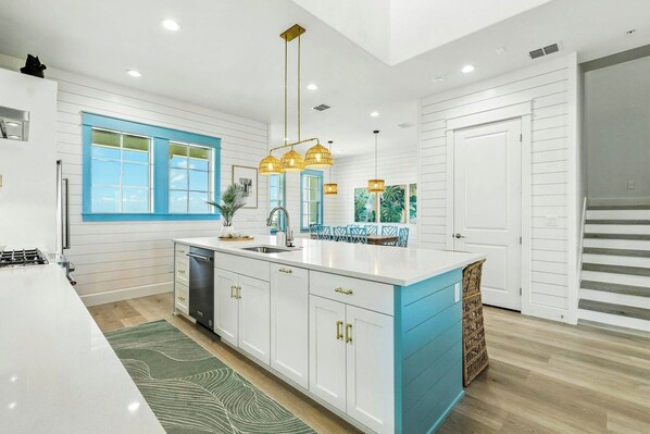 A modern kitchen with a central island, white cabinetry, and a blue accent wall. - Tequila Sunrise | Gulf Views | Private Elevator (Port Aransas)
