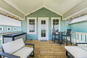 A covered porch with a wooden floor, two chairs, a table, and a dog. - Tequila Sunrise | Gulf Views | Private Elevator (Port Aransas)