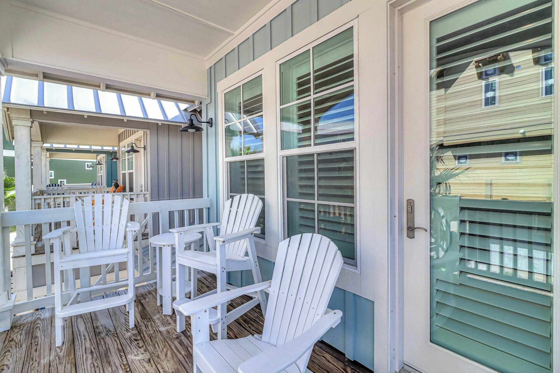A covered porch with white Adirondack chairs and a wooden deck.