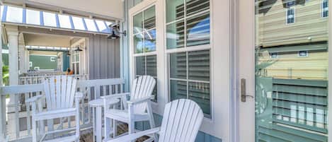 A covered porch with white Adirondack chairs and a wooden deck.