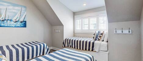 A bedroom with two beds, a painting of sailboats, a window with blinds, and a ceiling light.