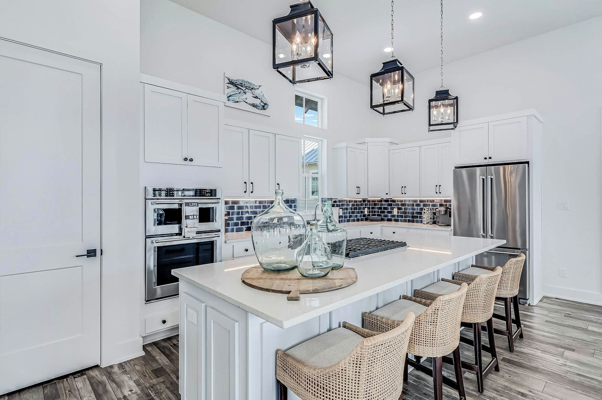 A modern kitchen with white cabinetry, a large island with bar stools, a stainless steel refrigerator, and pendant lighting.