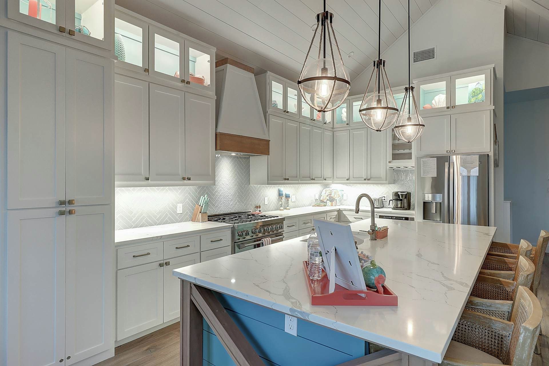 A modern kitchen with white cabinetry, a central island, stainless steel appliances, and pendant lighting.