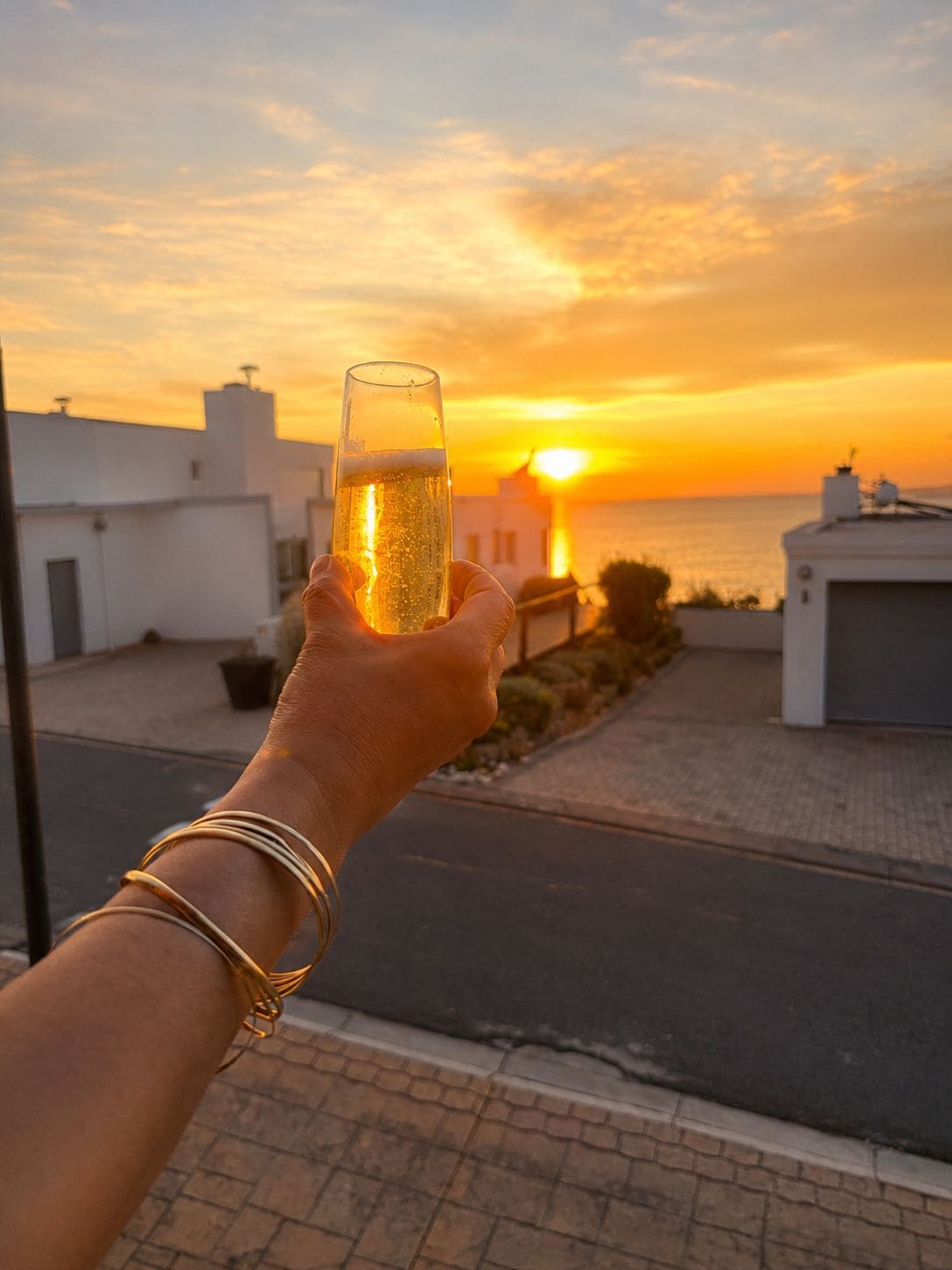 A hand holding a glass of beer with a sunset in the background.