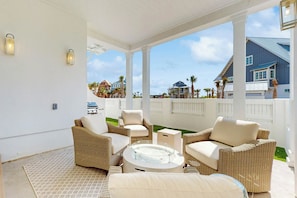 A covered outdoor seating area with wicker furniture and a glass-top table, overlooking a residential neighborhood. - Villa Palmilla | Steps to Beach | Game Room (Port Aransas)