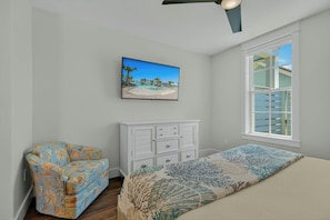A bedroom with a bed, a dresser, a chair, a television, and a window. - Palmilla Blue Ocean Blessing | Steps to Beach (Port Aransas)