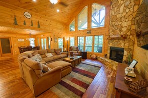 A cozy cabin interior with a large sectional sofa, a fireplace, and a stone accent wall. - Trail, 4BR, 2 King suites, Hot Tub, Pool Table & Firepit (Cherry Log)