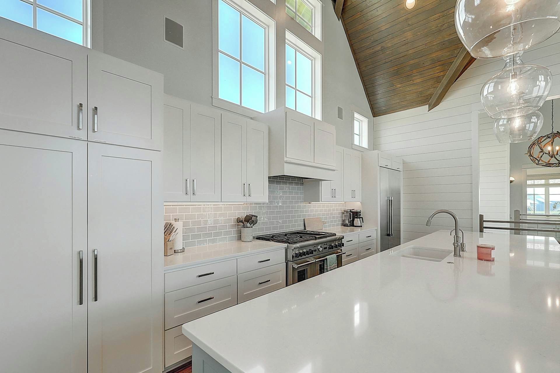 Une cuisine moderne avec des meubles blancs, un grand îlot central et un plafond en bois.