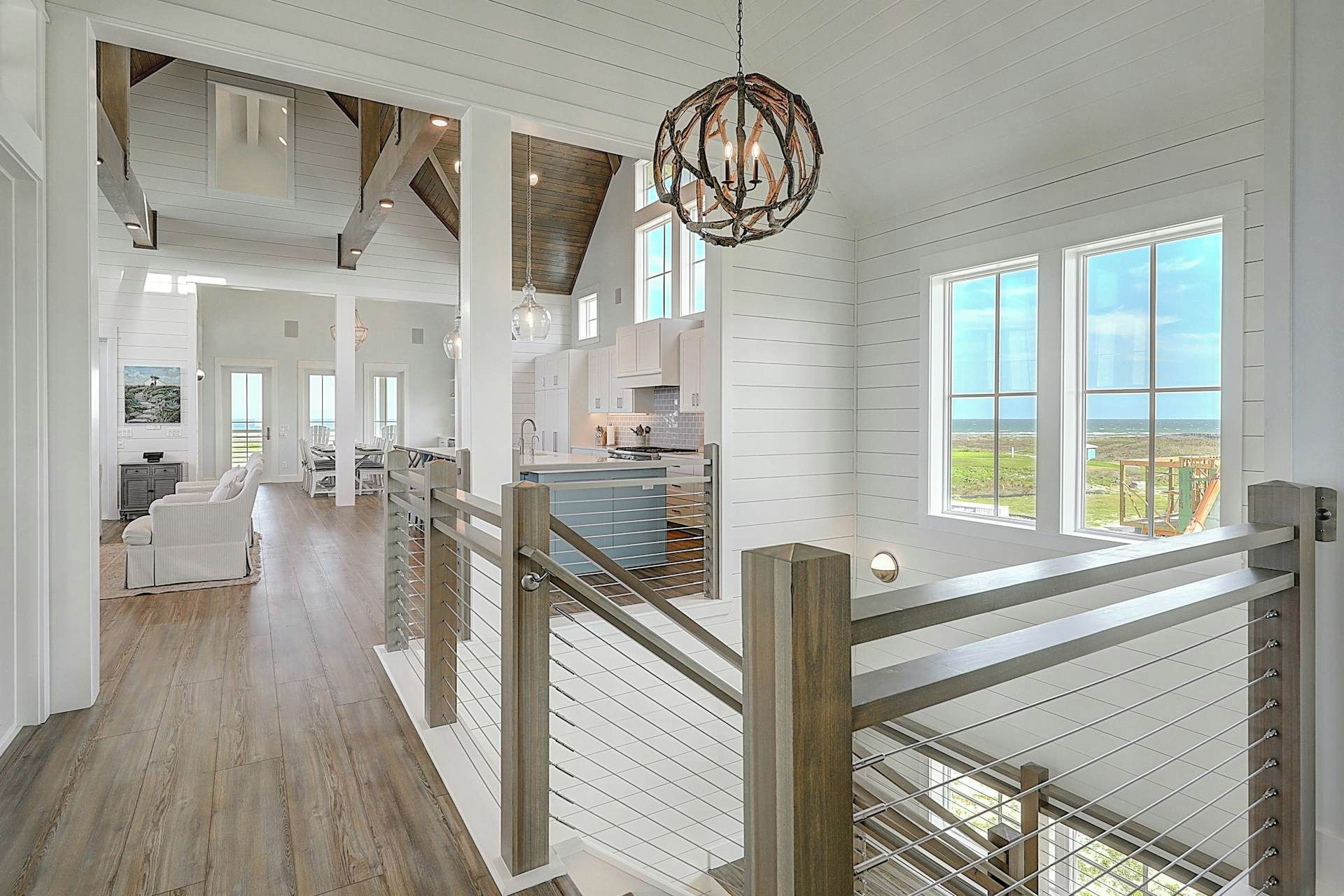 A spacious interior with a high ceiling, a staircase with a railing, and large windows offering a view.