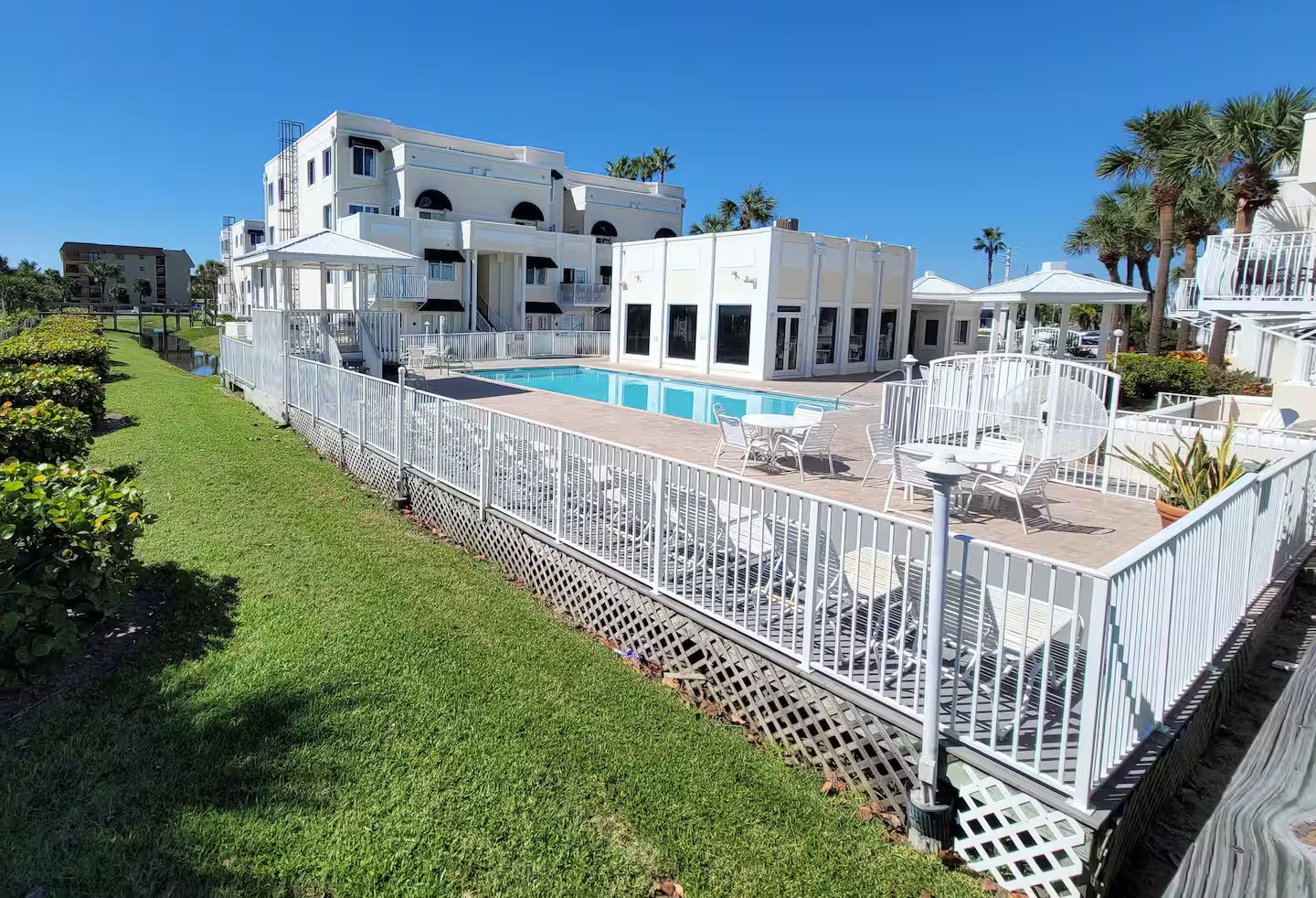 A hotel with a swimming pool, outdoor seating, and a white fence.