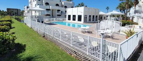 A hotel with a swimming pool, outdoor seating, and a white fence.