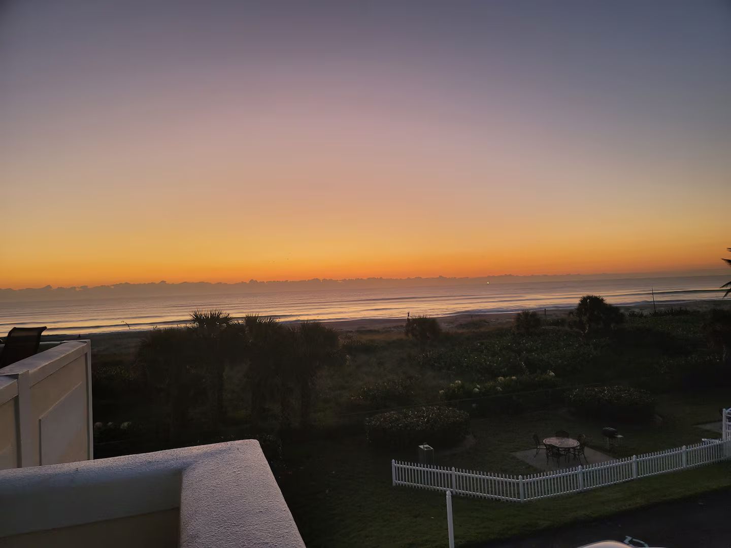 A balcony with a view of the ocean at sunset.