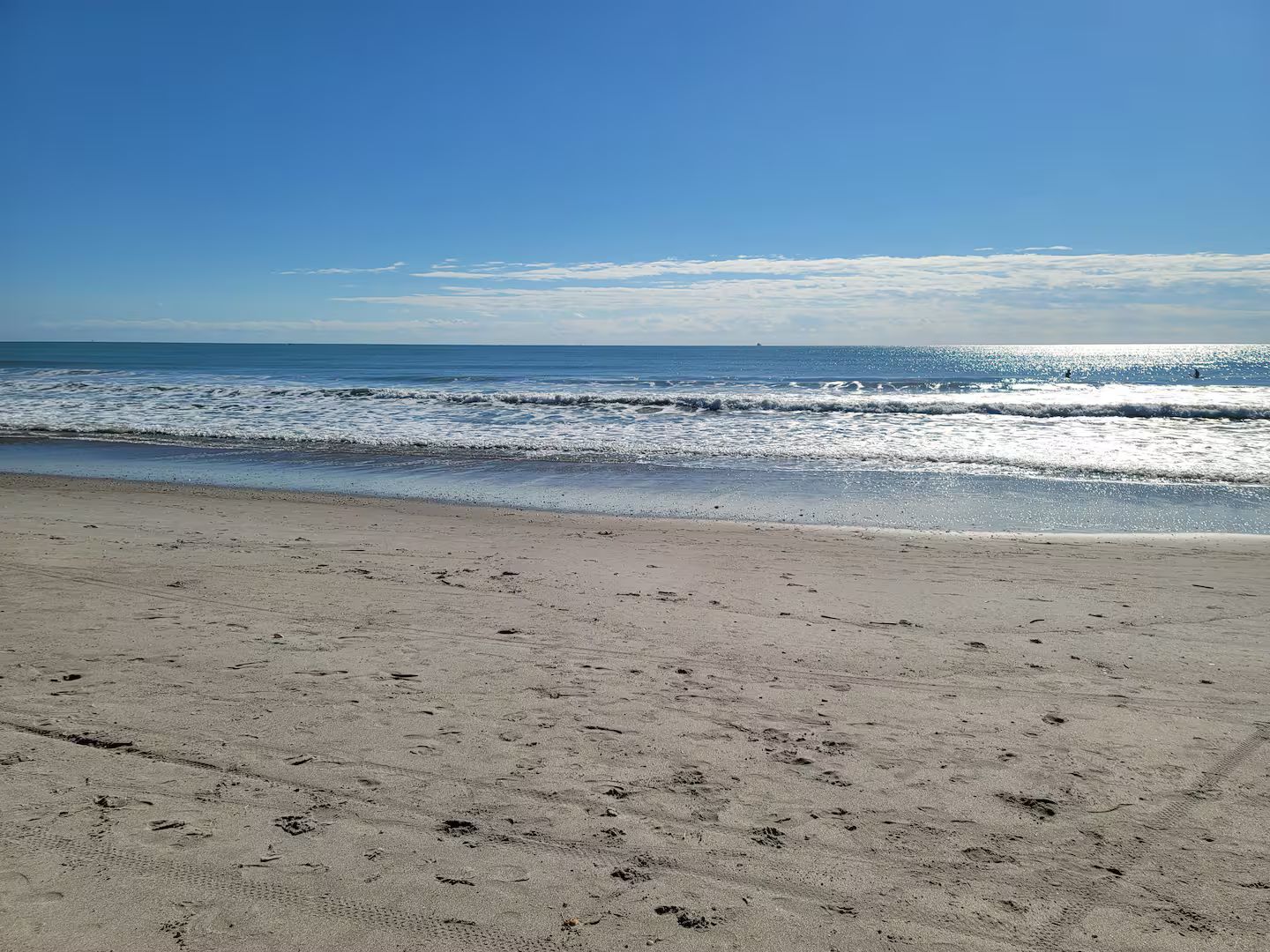 A beach with footprints in the sand and a clear sky.