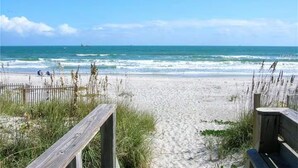 Een strand met een houten looppad naar het water, een bankje en een hek.