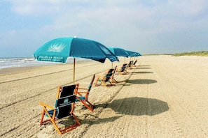 A beach with rows of beach chairs and umbrellas, some with 'PALMILLA BEACH' branding. - Real Good Tan | Golf Views | Steps to Beach (Port Aransas)