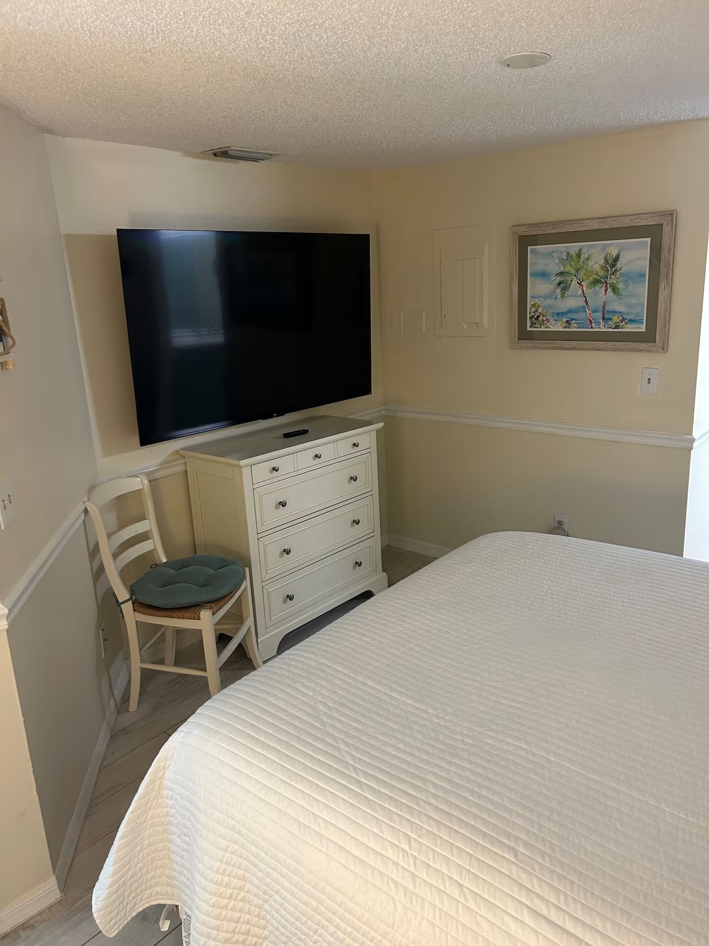 Ein Schlafzimmer mit einem Bett, einem Schminktisch, einem Stuhl, einem Fernseher und einem Bild an der Wand.