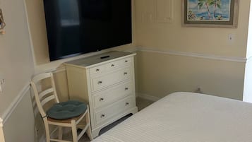 Ein Schlafzimmer mit einem Bett, einem Schminktisch, einem Stuhl, einem Fernseher und einem Bild an der Wand.