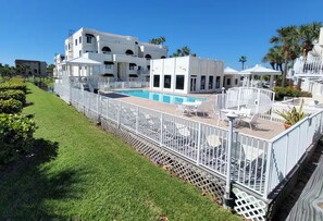 A hotel with a swimming pool, outdoor seating, and a white fence.