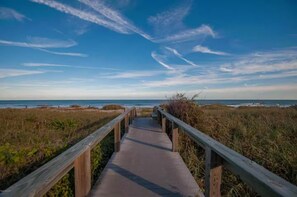A wooden boardwalk leading to a beach with dunes and a clear sky.