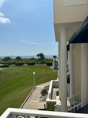 A balcony with a view of a well-maintained lawn and a distant body of water.