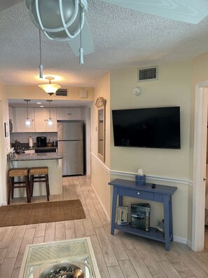 A modern kitchen with a built-in refrigerator, a dining area with a table and chairs, and a flat-screen TV mounted on the wall.