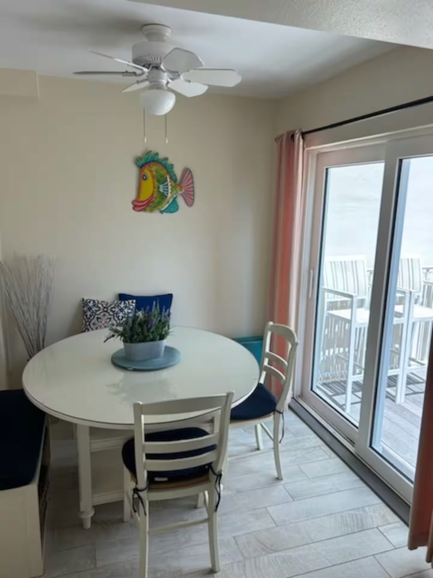Ein Essbereich mit einem runden Tisch, Stühlen, einem Deckenventilator und Blick durch ein großes Fenster.