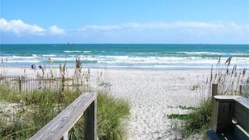 Ein Strand mit einer Holzpromenade, die zum Wasser führt, einer Bank und einem Zaun.