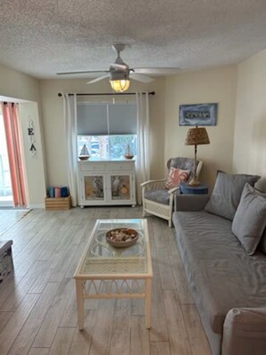 A living room with a ceiling fan, a glass coffee table, a sofa, and a chair.