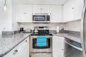 A kitchen with white cabinets, a stainless steel oven, a microwave, a toaster, and a kettle.