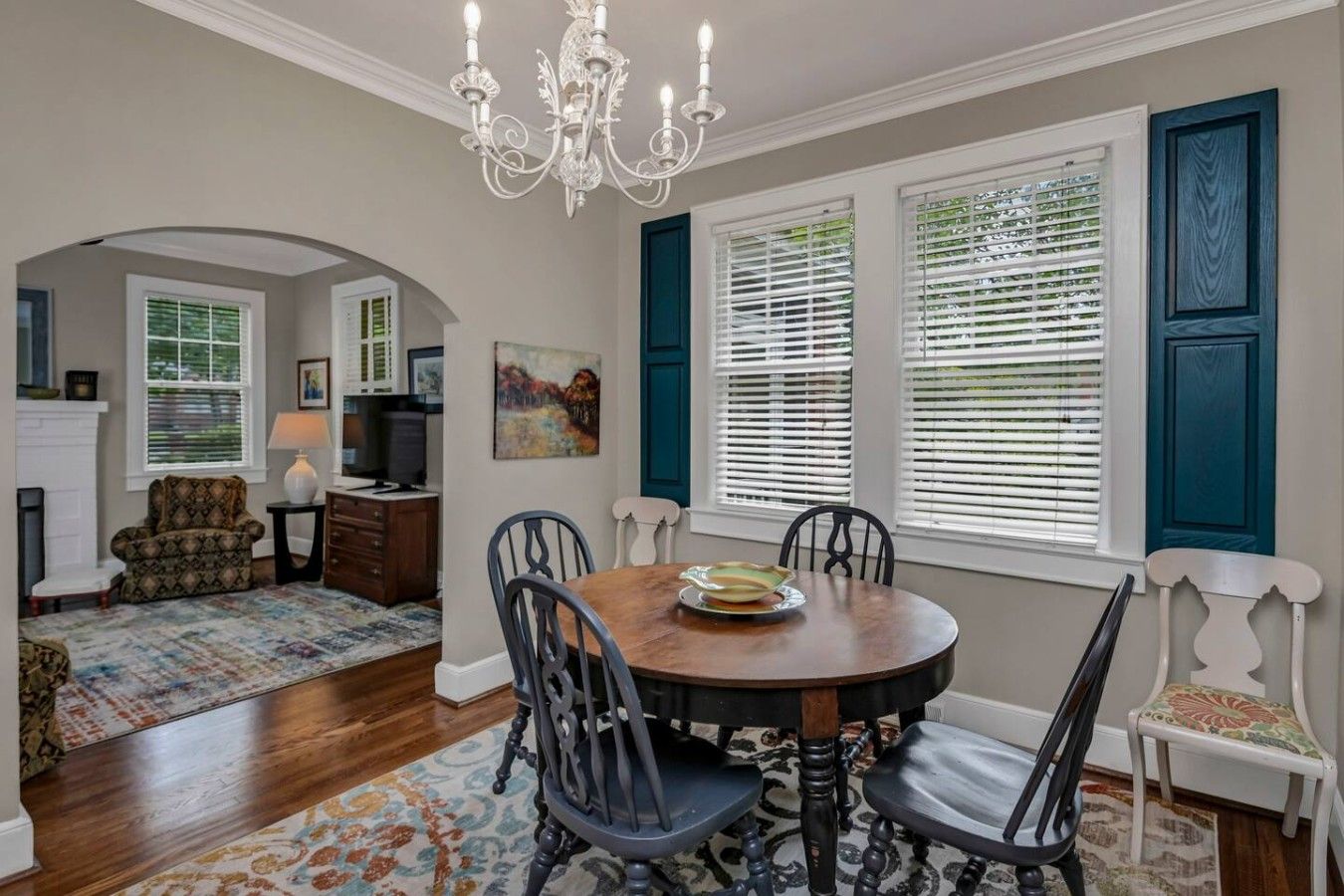 A dining area with a round table, chairs, a chandelier, and a fireplace.