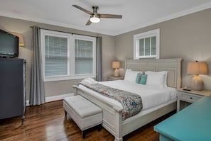 A bedroom with a bed, bedside lamps, a ceiling fan, a television, and a window with blinds. - WECO Getaway | Near USC + Downtown (West Columbia)