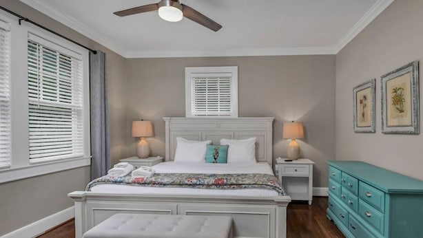 A bedroom with a large bed, bedside tables, a bench, a ceiling fan, and a dresser. - WECO Getaway | Near USC + Downtown (West Columbia)