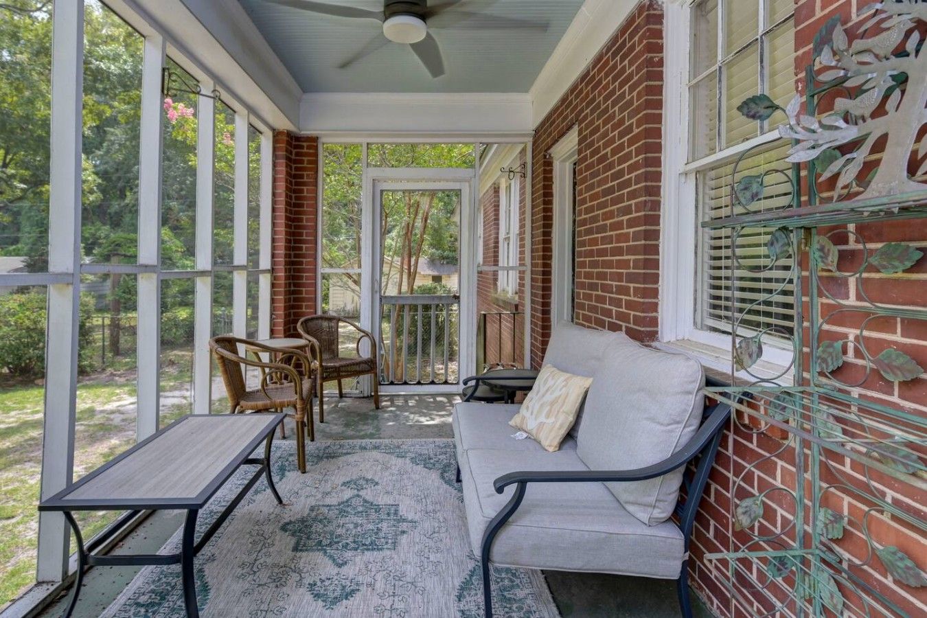 A covered porch with a table and chairs, a sofa, and a decorative metal fence.