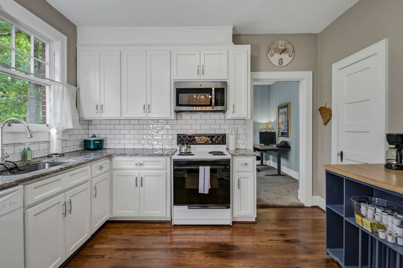 A kitchen with white cabinets, a microwave, an oven, and a sink.