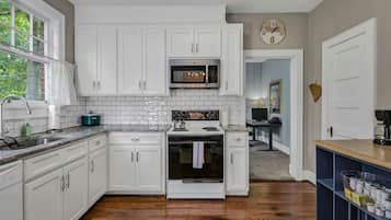 A kitchen with white cabinets, a microwave, an oven, and a sink.