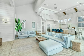 A spacious living room with a large L-shaped sofa, a coffee table, and a staircase leading to an upper level. - Sunny Daze | Gulf Views | Steps to Beach | Firepit (Port Aransas)