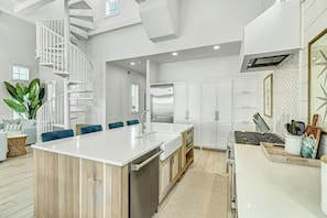 A modern kitchen with a central island, white cabinetry, and a spiral staircase. - Sunny Daze | Gulf Views | Steps to Beach | Firepit (Port Aransas)