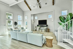 A spacious living room with a large sectional sofa, a flat-screen TV, and a staircase with a railing. - Sunny Daze | Gulf Views | Steps to Beach | Firepit (Port Aransas)