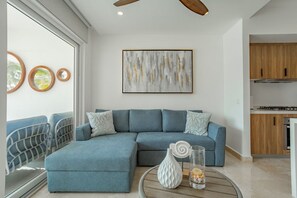 A modern living room with a sectional sofa, a glass coffee table, and a kitchen area with wooden cabinets. - Harbor 171 Beachfront  Walking Distance to the Malecón (Puerto Vallarta)