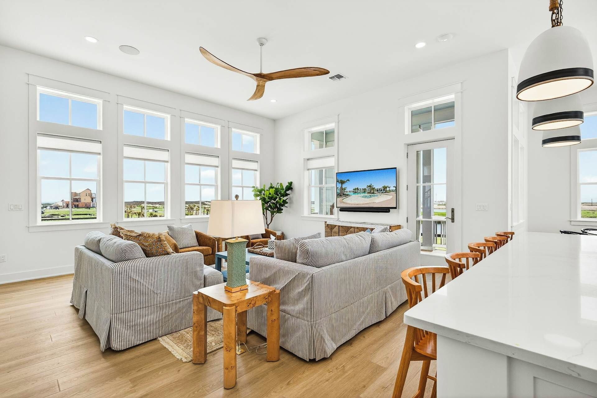 A spacious living room with a large sofa set, a dining area with wooden chairs, and a kitchen island.