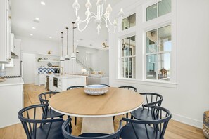 A modern kitchen with white cabinetry, a central island, and a chandelier. - Sunset Hacienda | Water Views | Steps to Beach (Port Aransas)