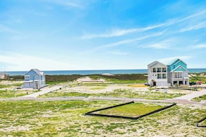 A beachfront property with multiple houses, a clear sky, and a sandy landscape. - Sunset Hacienda | Water Views | Steps to Beach (Port Aransas)