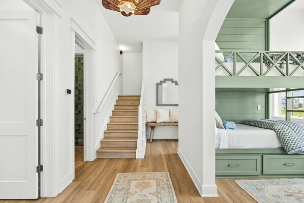 A staircase leading to a bedroom with a bunk bed, a small seating area, and a decorative mirror. - Sunset Hacienda | Water Views | Steps to Beach (Port Aransas)