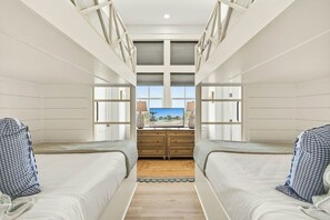 A room with two beds, a TV, and a window with a view of palm trees. - Sunset Hacienda | Water Views | Steps to Beach (Port Aransas)