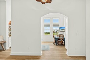 A bright hallway with white walls, a wooden floor, and a dining area with a table and chairs. - Sunset Hacienda | Water Views | Steps to Beach (Port Aransas)